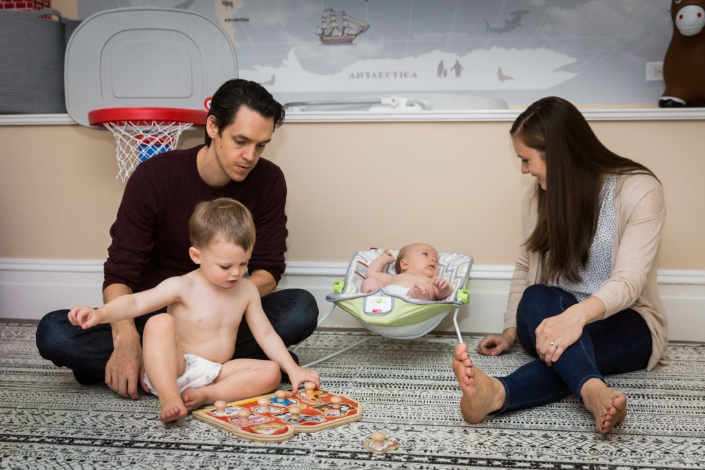Parents playing on carpet with two young sons for an article on how to prepare for a newborn portrait session