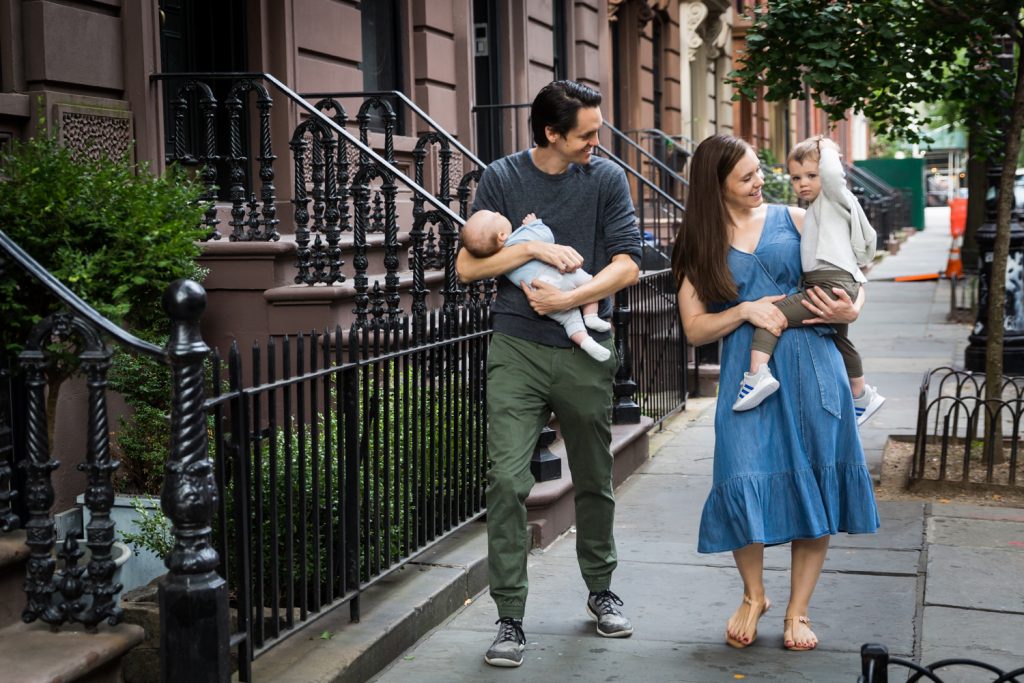 Parents holding two young sons walking down NYC sidewalk for an article on how to prepare for a newborn portrait session