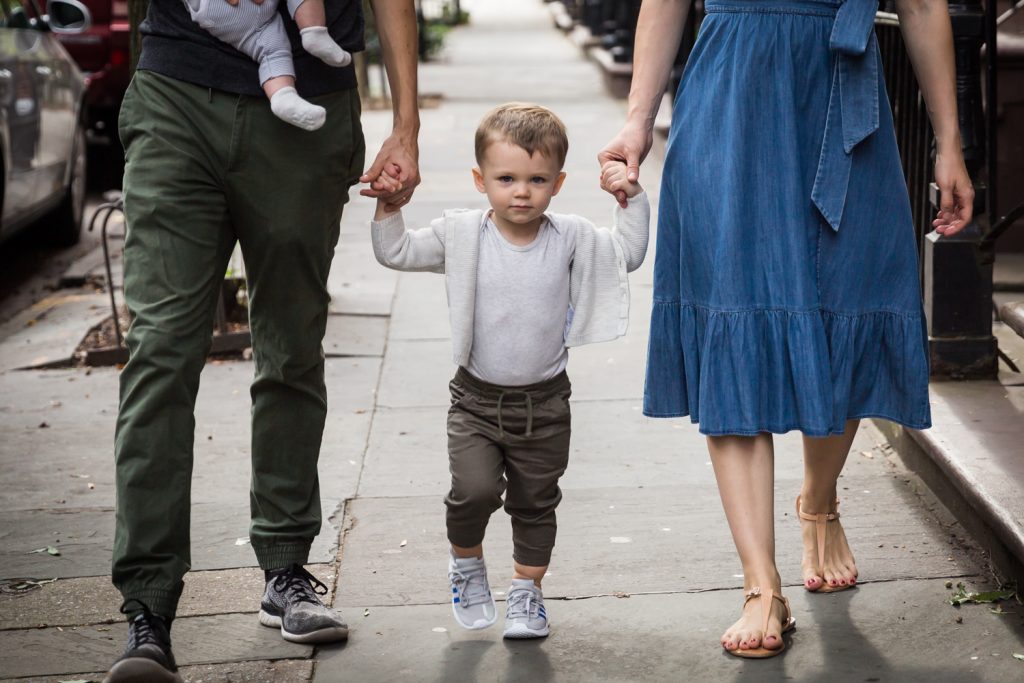 Young boy holding parents' hands on sidewalk