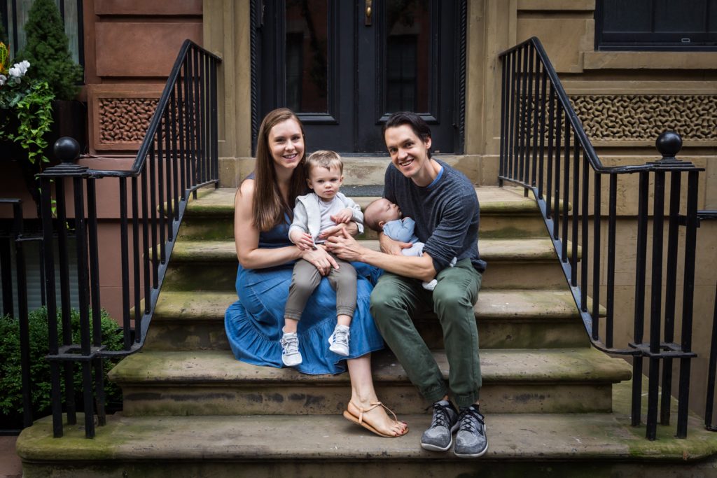 Parents with two young sons sitting on stoop for an article on how to prepare for a newborn portrait session