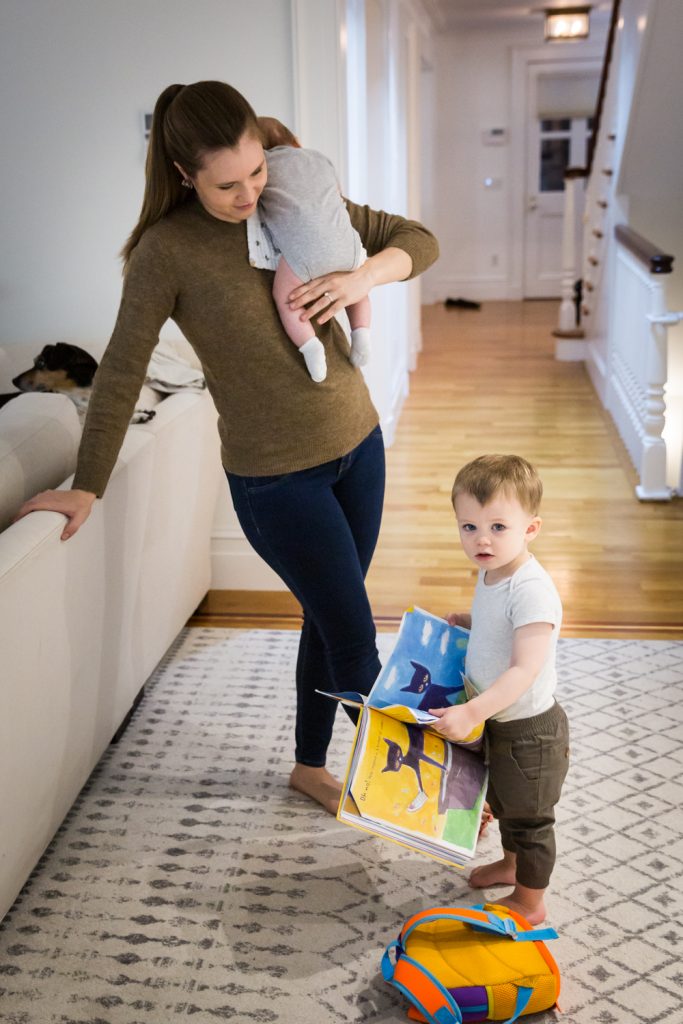 Mother holding newborn and watching toddler holding book