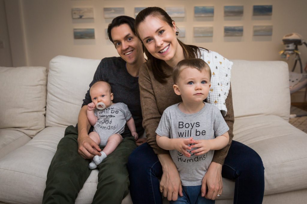 Parents with two young sons on couch for an article on how to prepare for a newborn portrait session