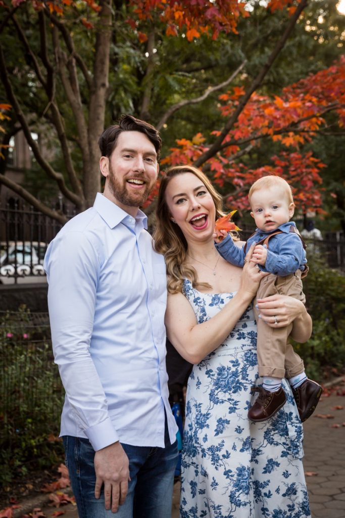 Parents holding baby son in front of tree with red leaves during a Marcus Garvey Park family portrait session