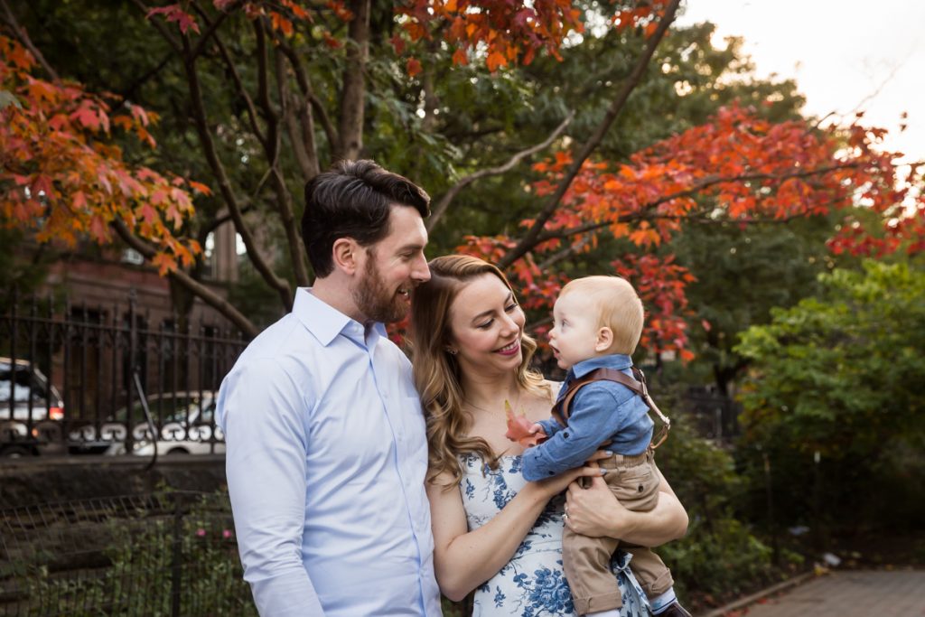Parents holding baby under tree with red leaves during a Marcus Garvey Park family portrait session