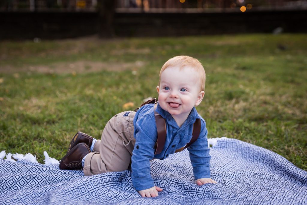 Baby boy wearing suspenders and crawling on blue blanket in Marcus Garvey Park