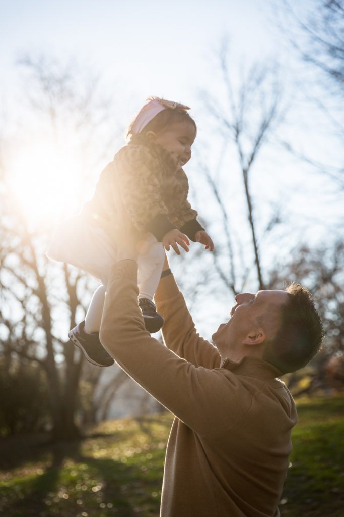 Father lifting little girl in the air for an article on Central Park holiday portrait tips