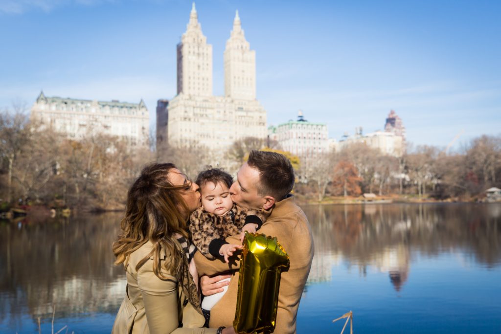 Parents kissing little girl's cheeks in front of Central Park Lake