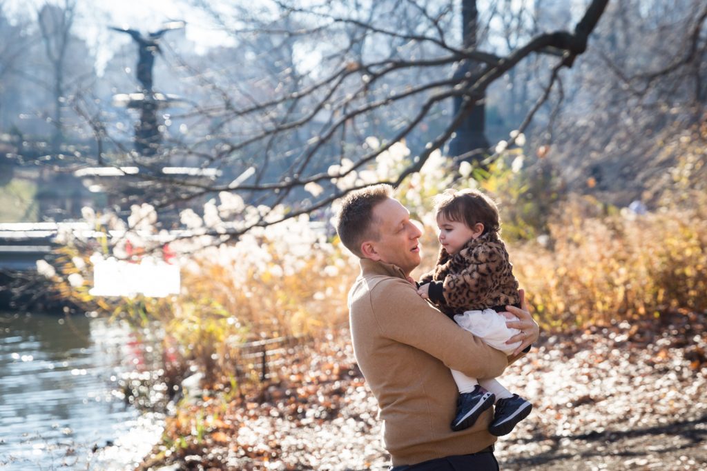 Father holding little girl with Bethesda Fountain in background for an article on Central Park holiday portrait tips