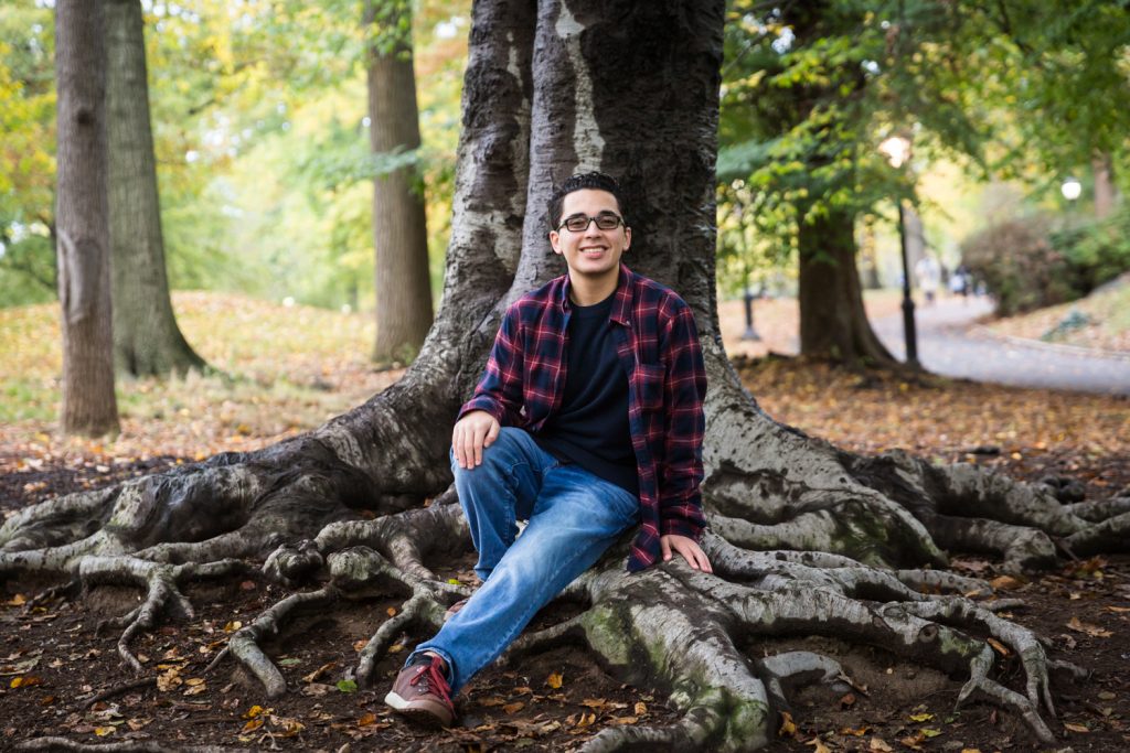 Young man sitting on tree roots during a Central Park senior portrait session