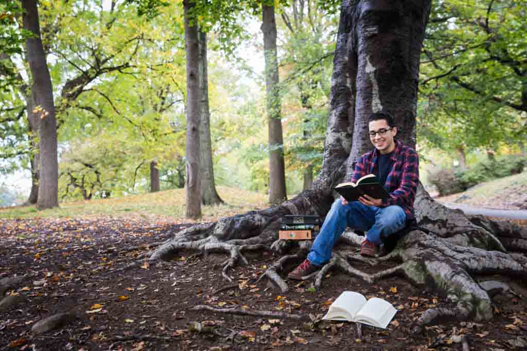 Young man under tree reading during a Central Park senior portrait session