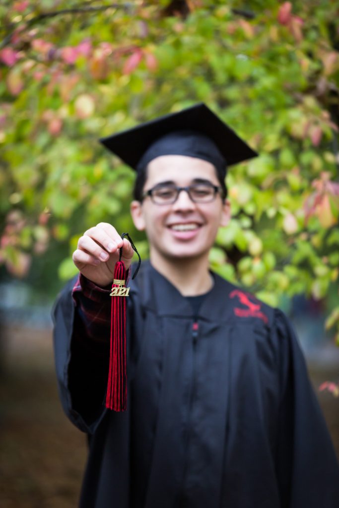 Young man holding out graduation tassle during a Central Park senior portrait session