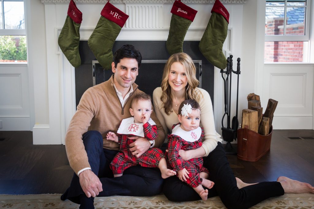 Parents holding baby twins in front of a fireplace for an article on holiday family portrait ideas