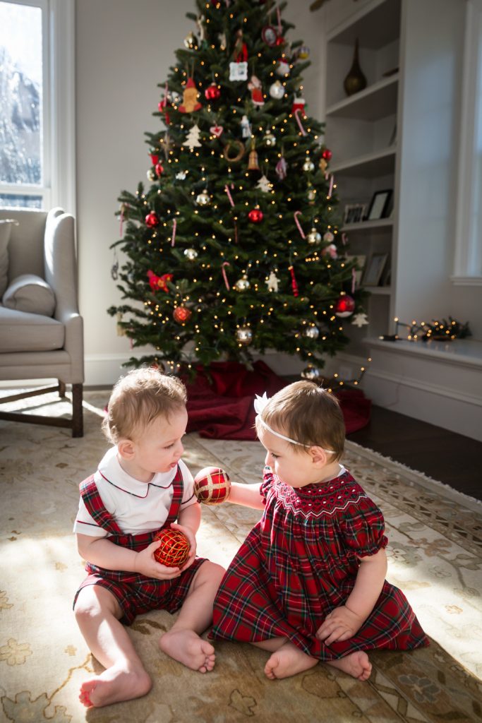 Two babies sitting on floor in front of Christmas tree