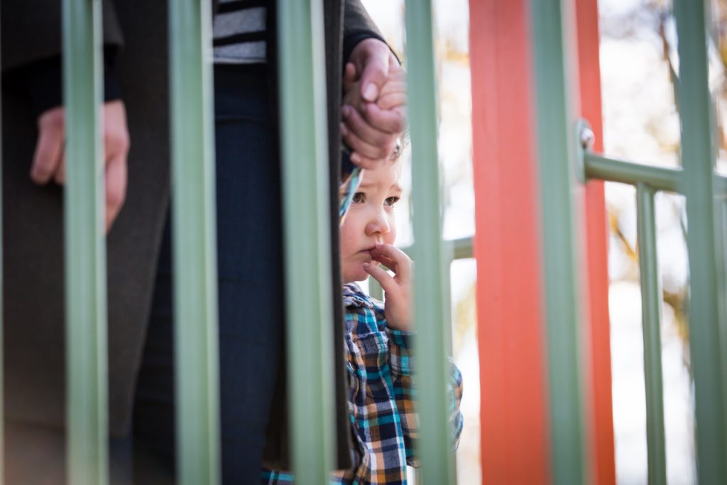 Nervous little boy seen through playground railing