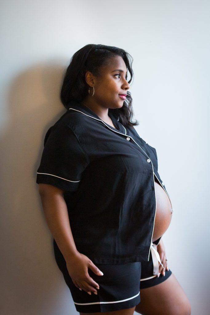 Pregnant woman standing against wall for an article on indoor maternity photo shoot tips