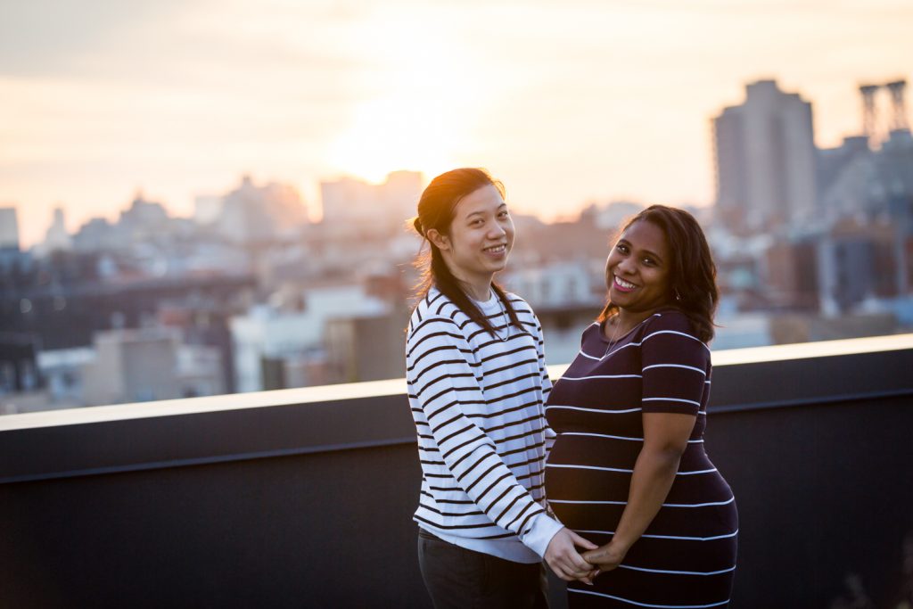 Couple holding hands on roof at sunset during maternity portrait photo shoot