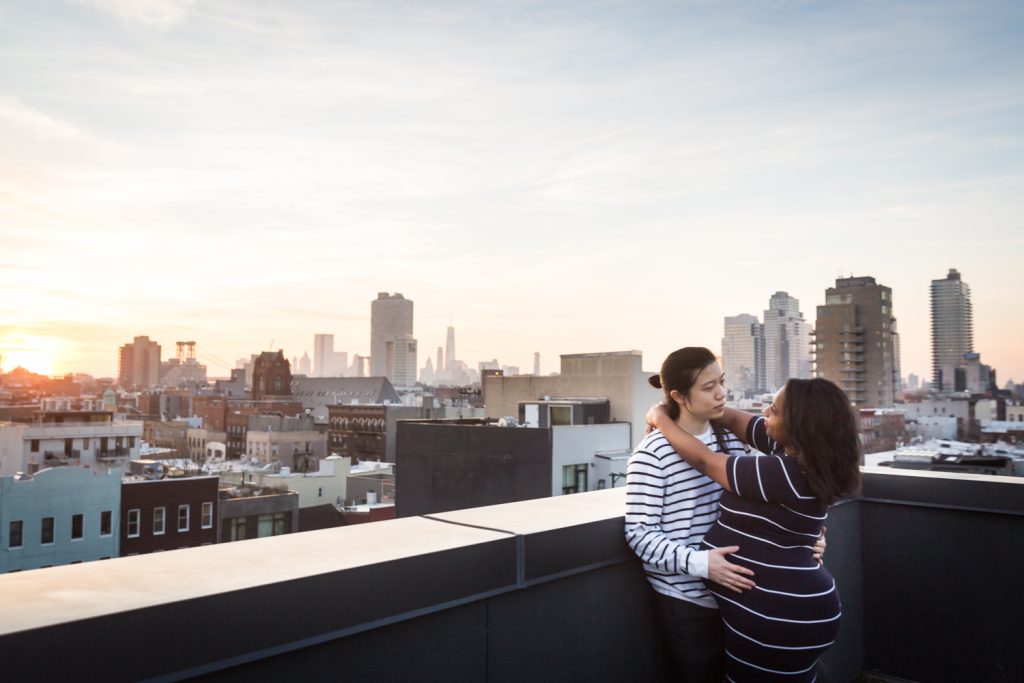 Couple hugging in corner of Brooklyn rooftop with view of NYC