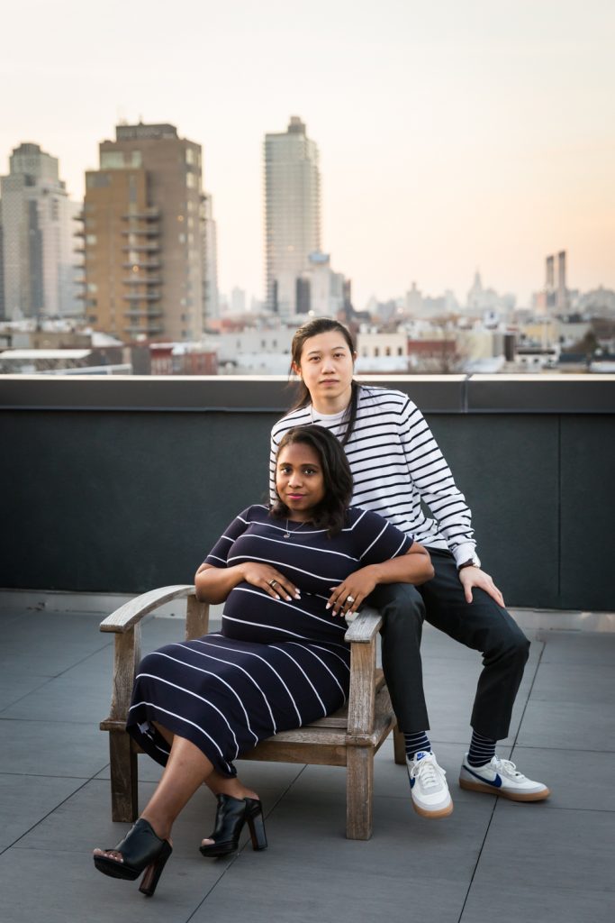 Couple posed against chair on Brooklyn rooftop during maternity portrait photo shoot