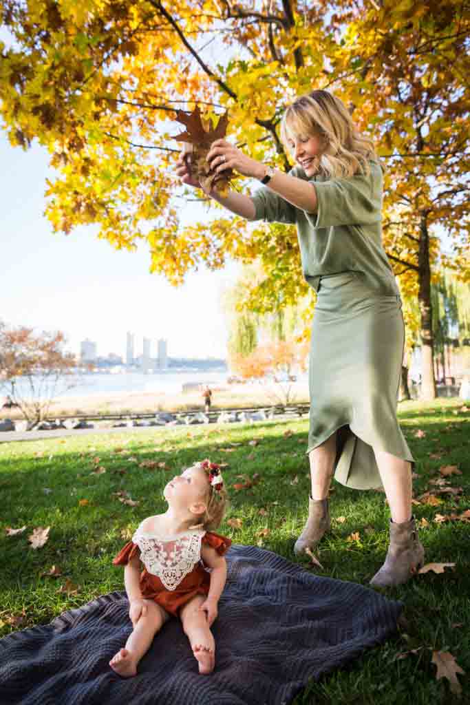 Mother dropping fall leaves down on little girl in Riverside Park