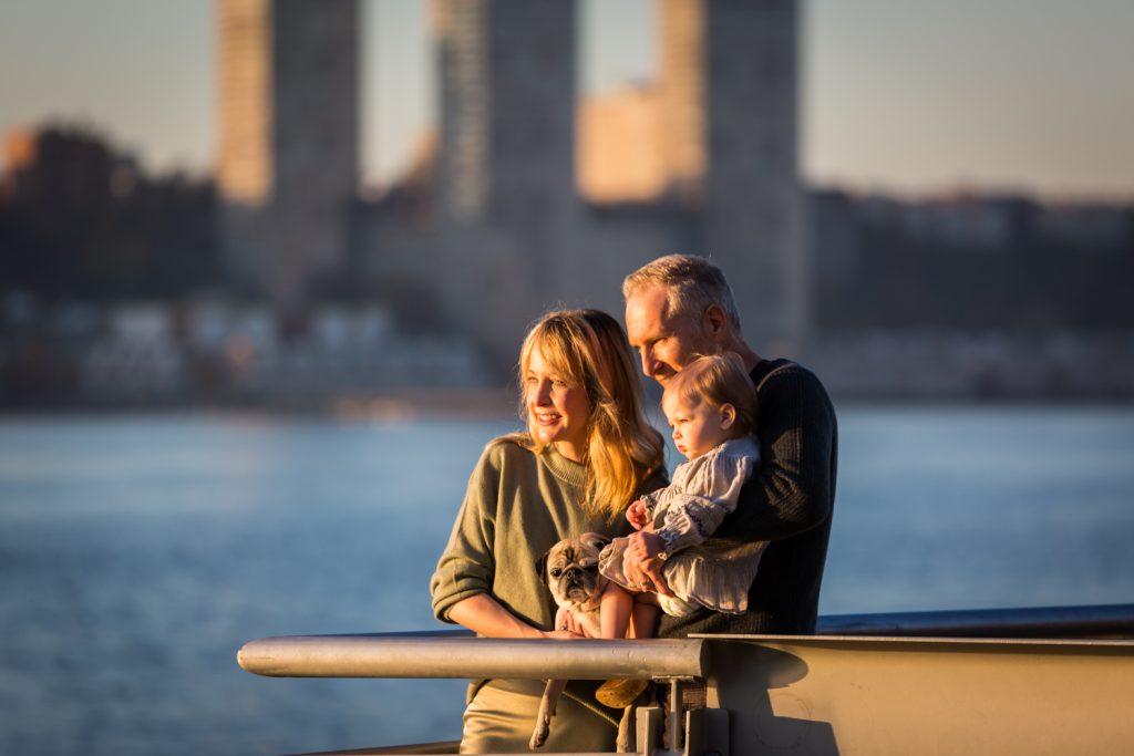 Parents holding little girl and dog on pier for an article NYC golden hour portrait tips