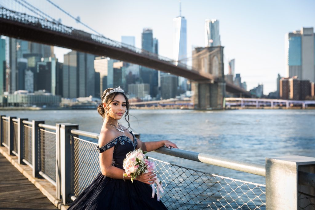 Girl wearing tiara and holding railing with Brooklyn Bridge in background