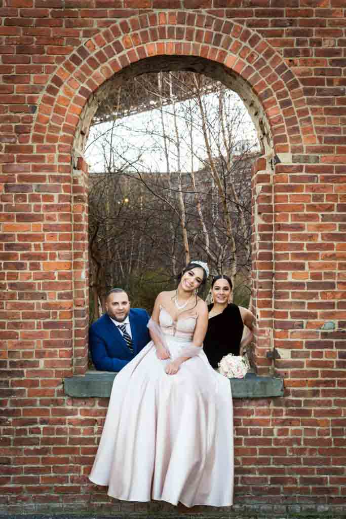 Girl in pink ball gown posing with parents under brick arch