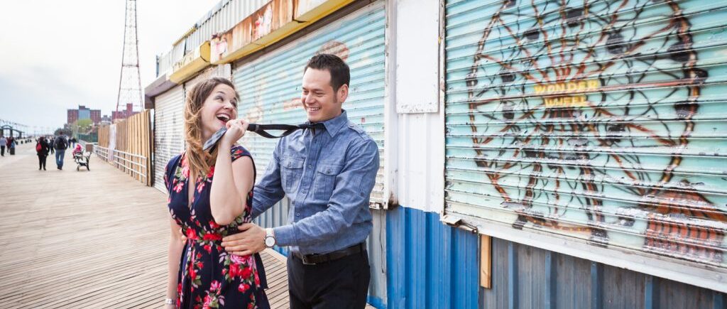 Woman pulling man by his tie on boardwalk or an article on Coney Island engagement photo tips
