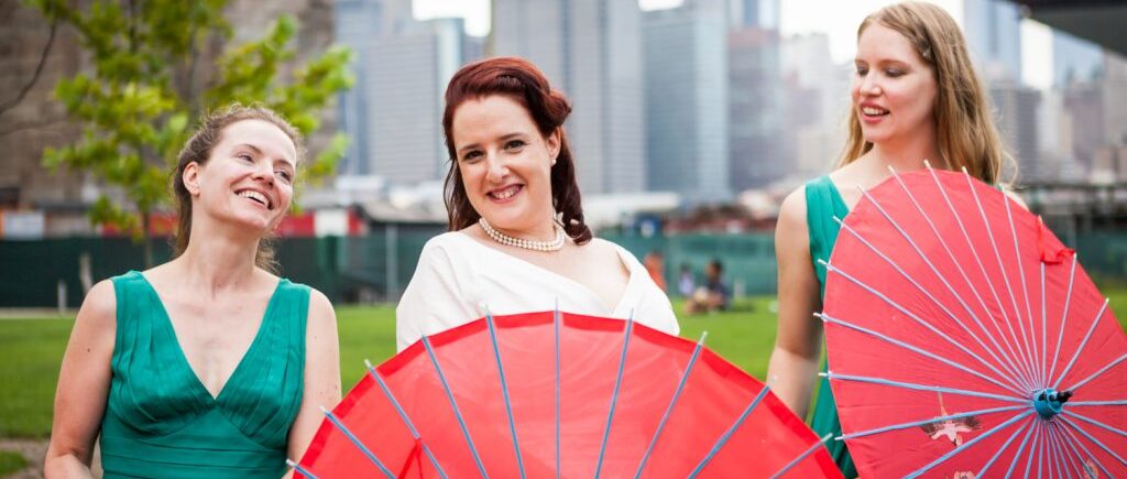 Bride and two bridesmaids with red umbrellas at a DUMBO wedding
