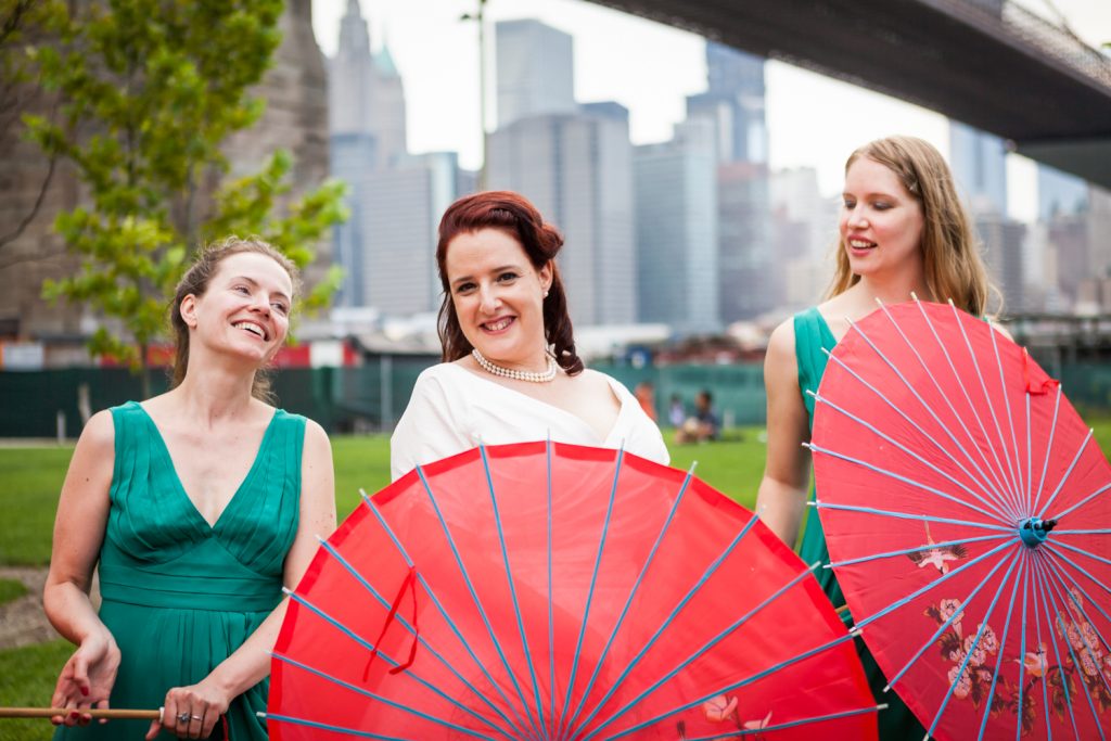 Bride and two bridesmaids with red umbrellas at a DUMBO wedding
