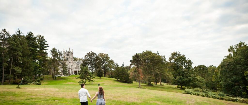Couple holding hands and walking across field during a Lyndhurst Mansion engagement session