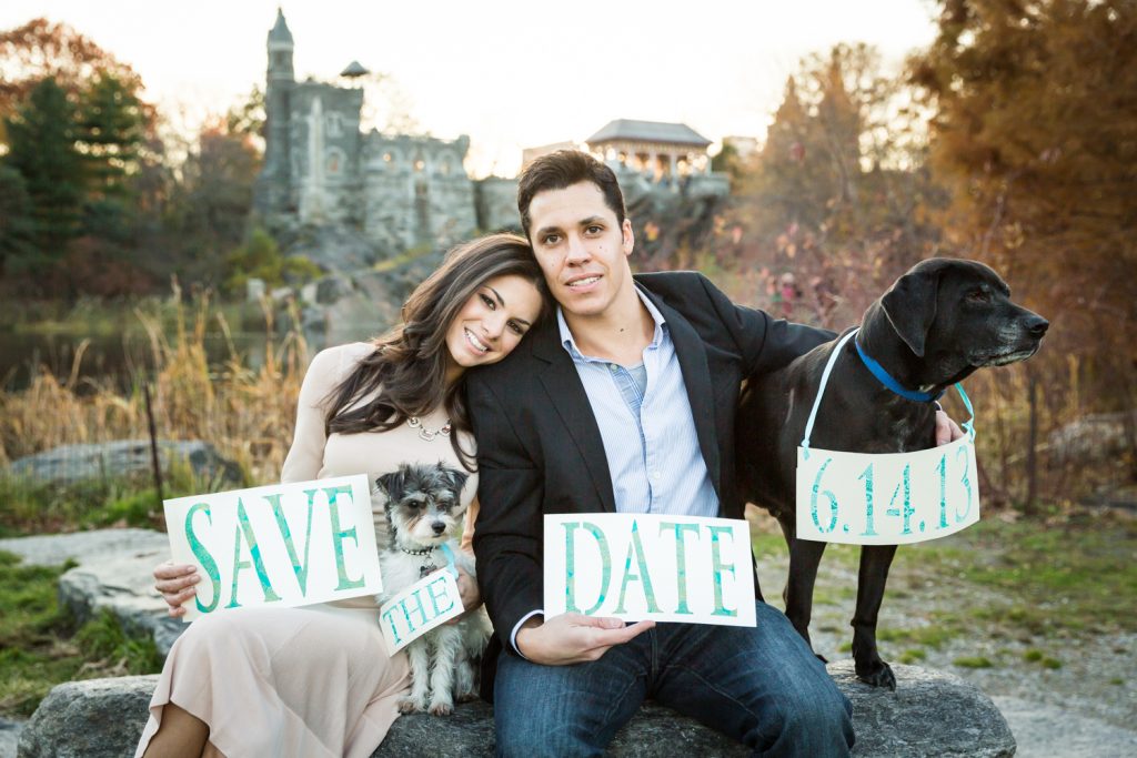 Central Park save-the-date photos of couple sitting on rock with two dogs holding sign