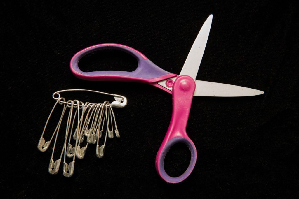 Scissors and safety pins from a photography emergency kit on black background