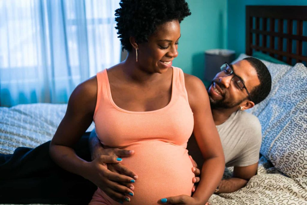 Parents-to-be sitting on bed for a Queens maternity photo shoot