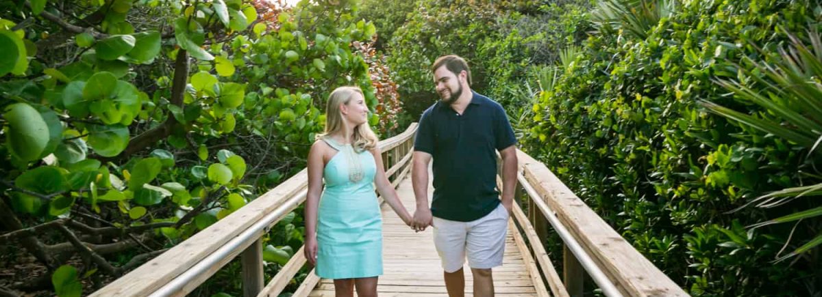 Couple holding hands and walking on boardwalk during a Coral Cove Park engagement shoot