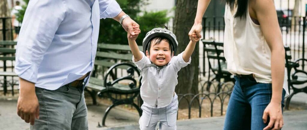 Chelsea family portrait of parents swinging little boy wearing bike helmet