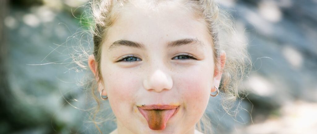 Little girl holding out colored tongue Family portrait in Central Park for an article on how to get natural smiles out of children