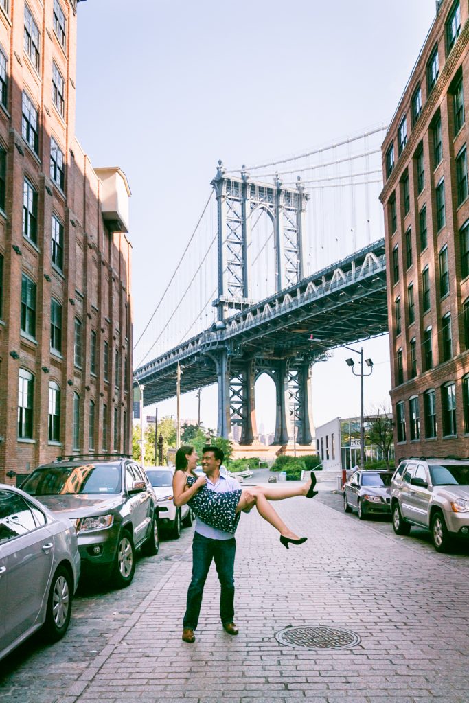 Man carrying woman in front of Manhattan Bridge