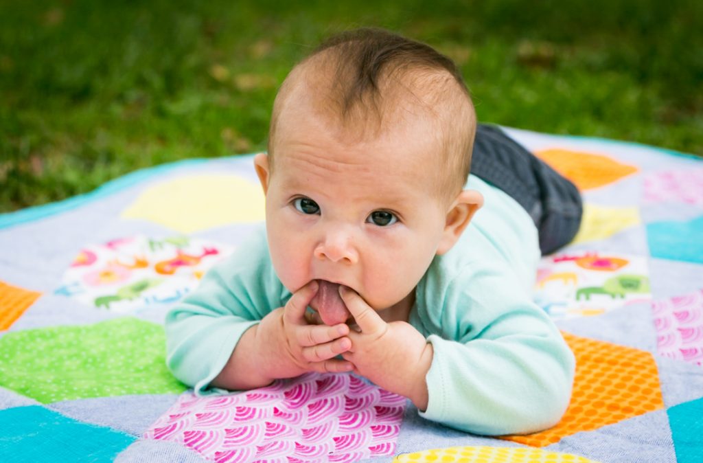 Baby on quilt with hands in mouth