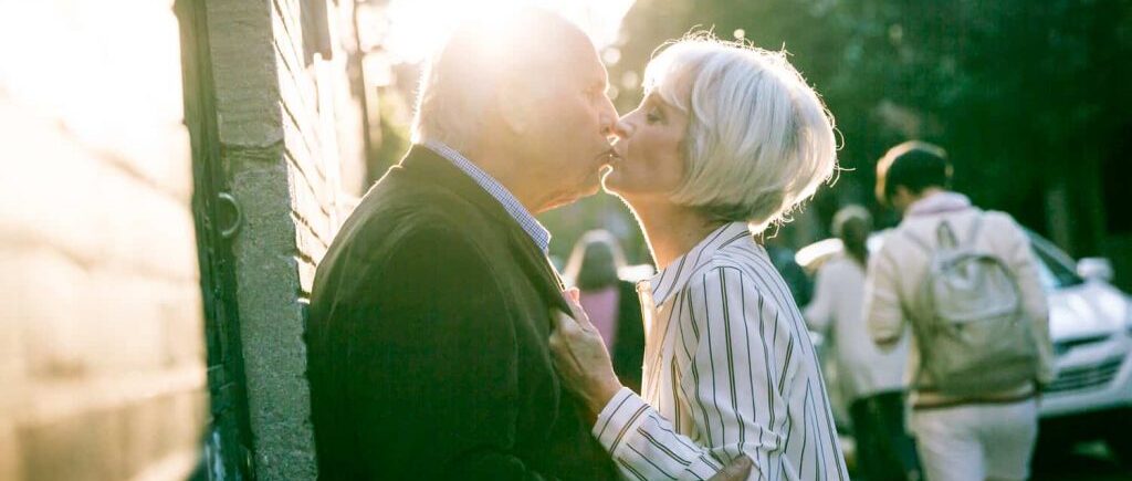 Photojournalistic portraits of older couple kissing against building