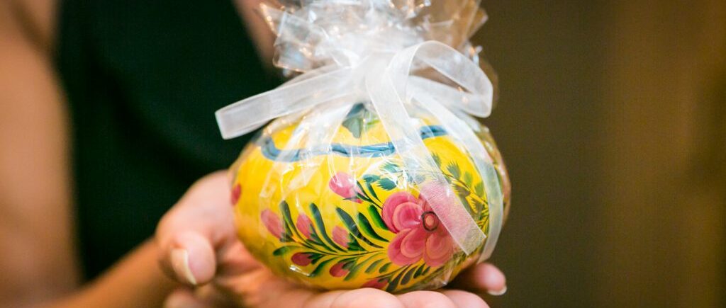 Hand holding colorfully-painted bomboniere wrapped in plastic for article on creative guest favors