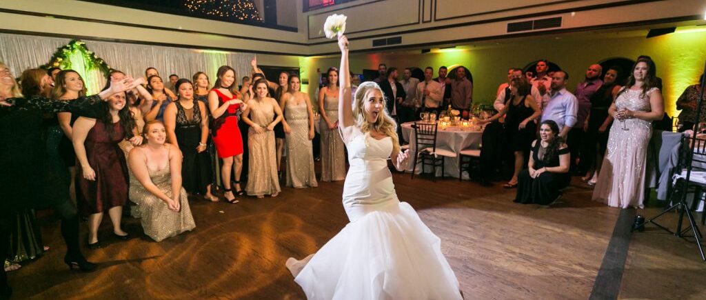 Bride with arm up about to throw bouquet at group of women for an article on how DJ lighting affects your wedding photos