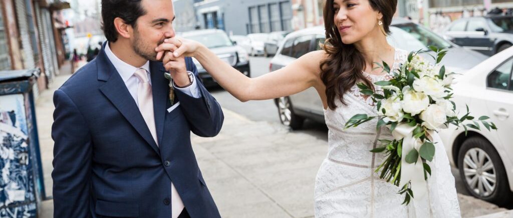 Groom kissing bride's hand on Brooklyn sidewalk