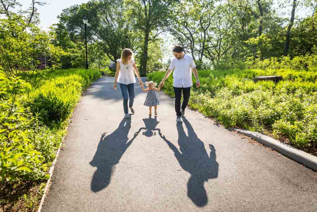 Parents holding hands with little girl in Forest Park for an article on toddler portrait tips