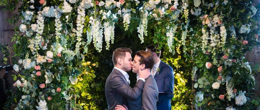 Greenpoint Loft wedding photos of two grooms kissing under gigantic floral altarpiece