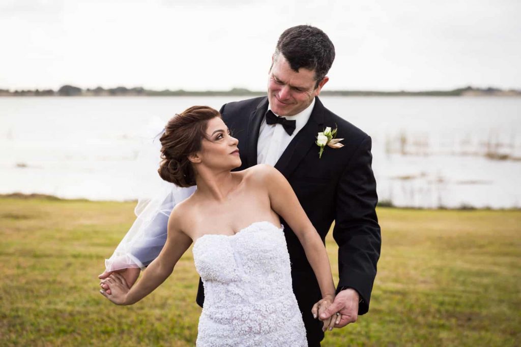 Bride and groom holding hands in front of lake for an article on wedding cost cutting tips