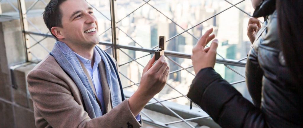 Man on one knee holding ring making a proposal on top of the Empire State Building