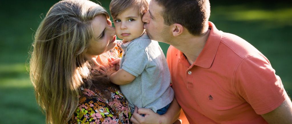 Parents kissing boy on cheeks during a Chelsea Waterside Park family portrait session