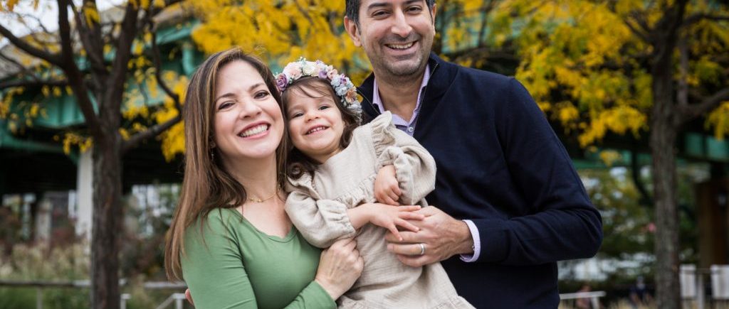Parents and little girl under yellow trees during a Riverside Park family portrait session