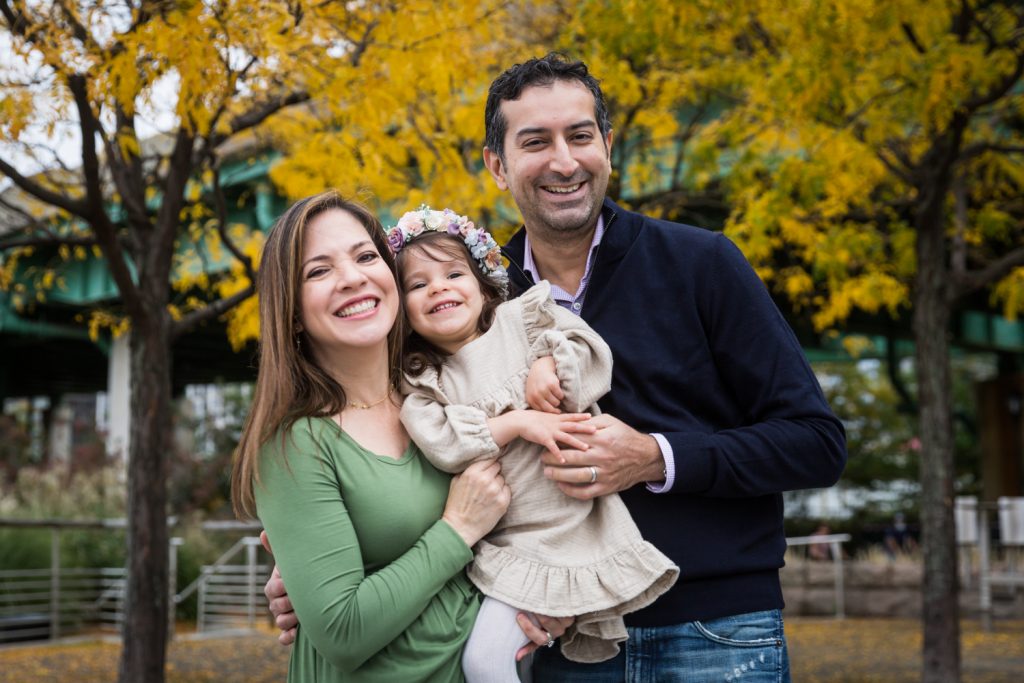 Parents and little girl under yellow trees during a Riverside Park family portrait session