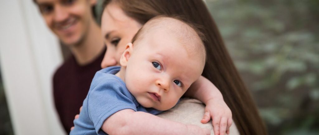 Mother holding newborn baby over shoulder for an article on how to prepare for a newborn portrait session